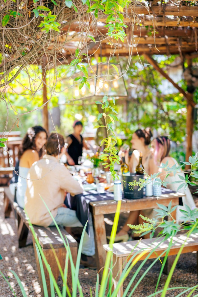 Friends sharing lunch and wine under a vine-covered pergola